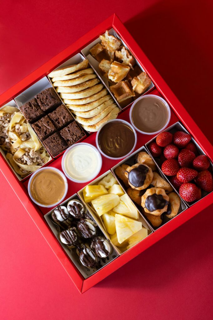 Brightly colored dessert assortment with fruits and dips in red box. Perfect for parties or gifting.